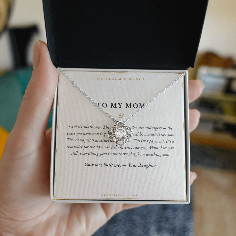 Hand holding open gift box with To My Mom message card and love knot necklace